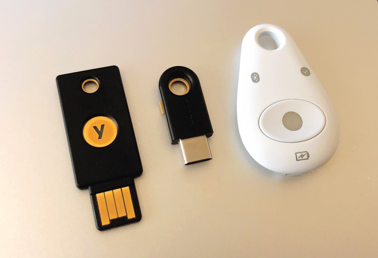 Tre chiavi hardware per l’autenticazione, due YubiKey nere e un token Feitian bianco, appoggiate su una superficie chiara.
