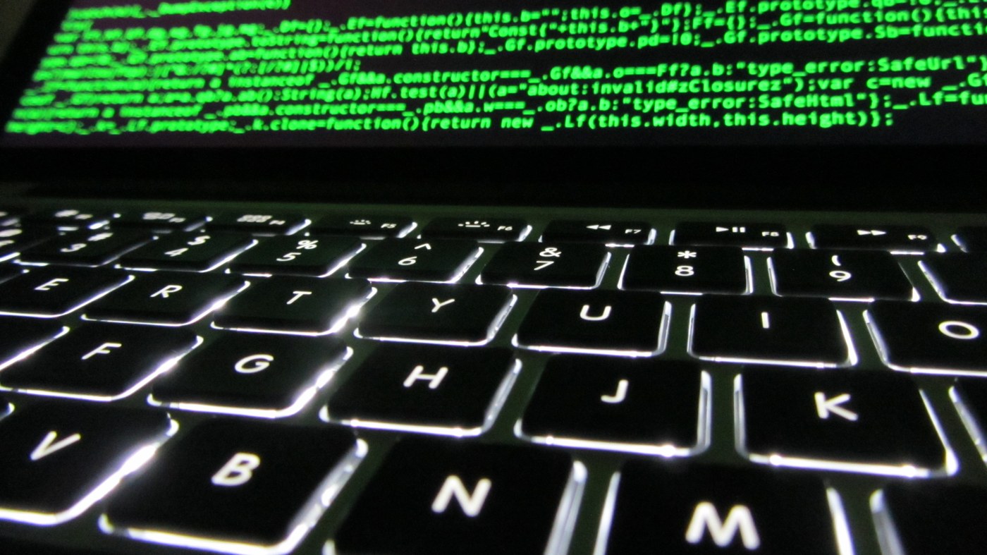 A laptop keyboard with JavaScript code visible on its screen.