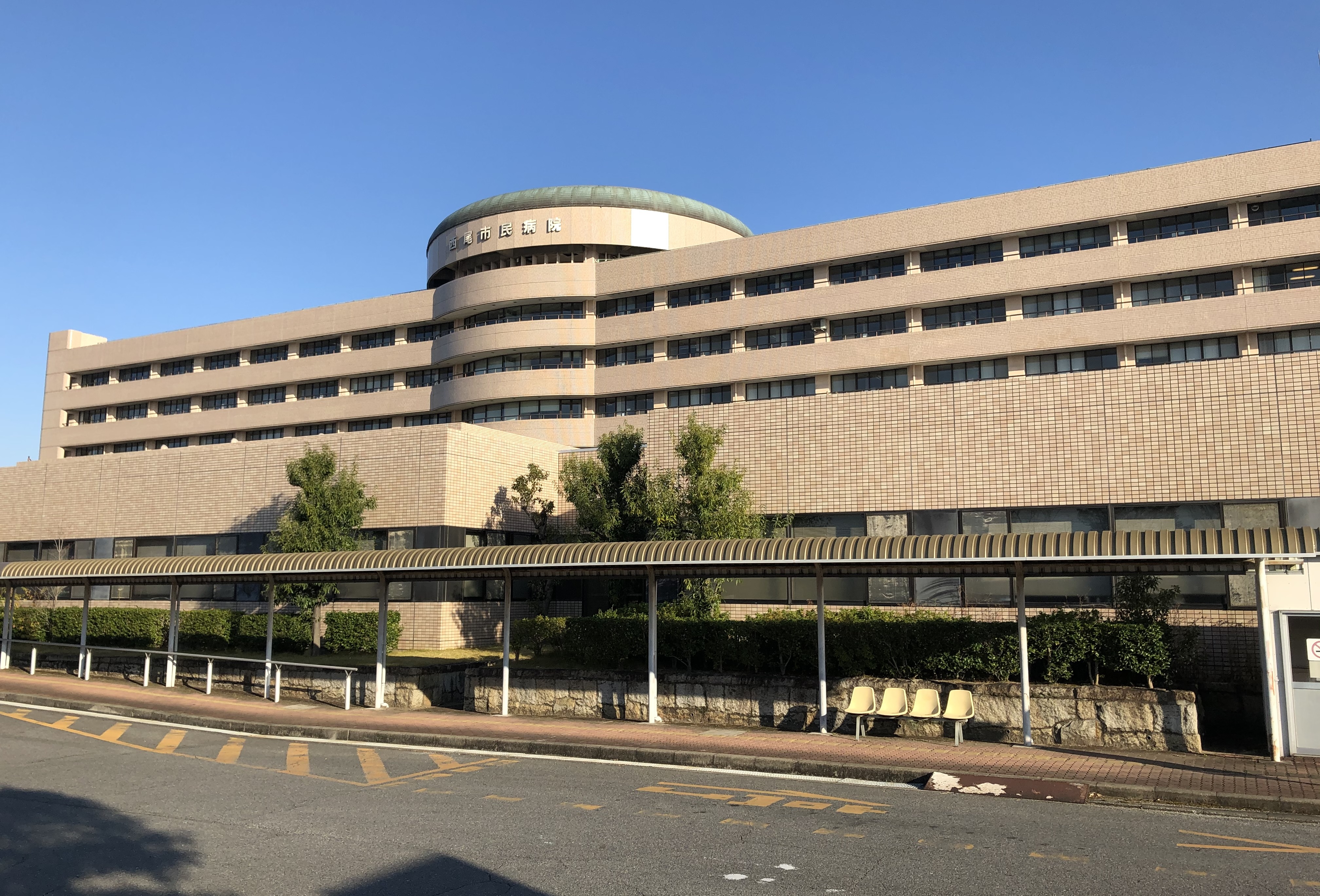 Facciata dell’ospedale municipale di Nishio, Giappone, con ingresso coperto e cielo azzurro; fotografia illustrativa.